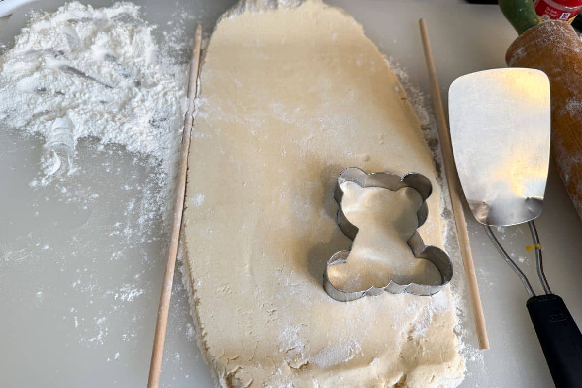 sugar cookie dough rolled between wooden dowel rods and cut with a teddy bear cookie cutter