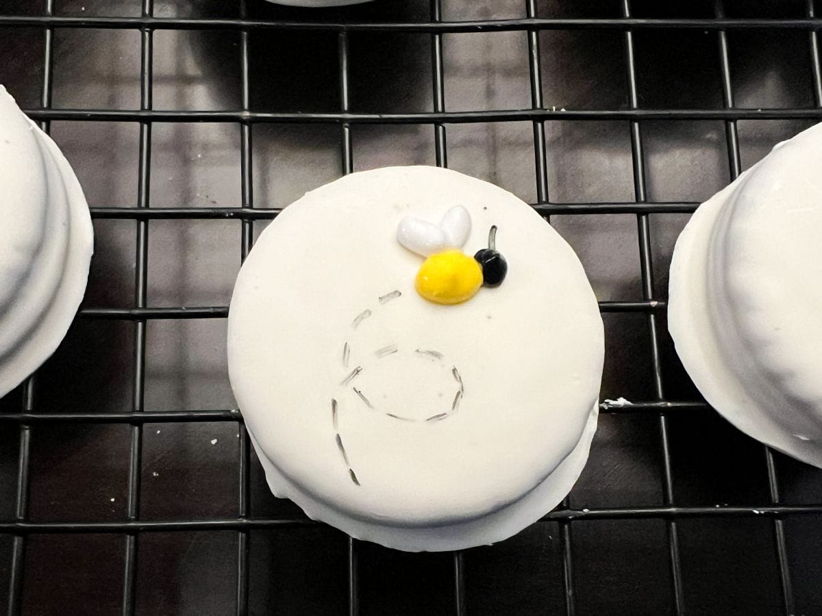 a royal icing bee with a black dotted path on a white fudge covered Oreo cookie
