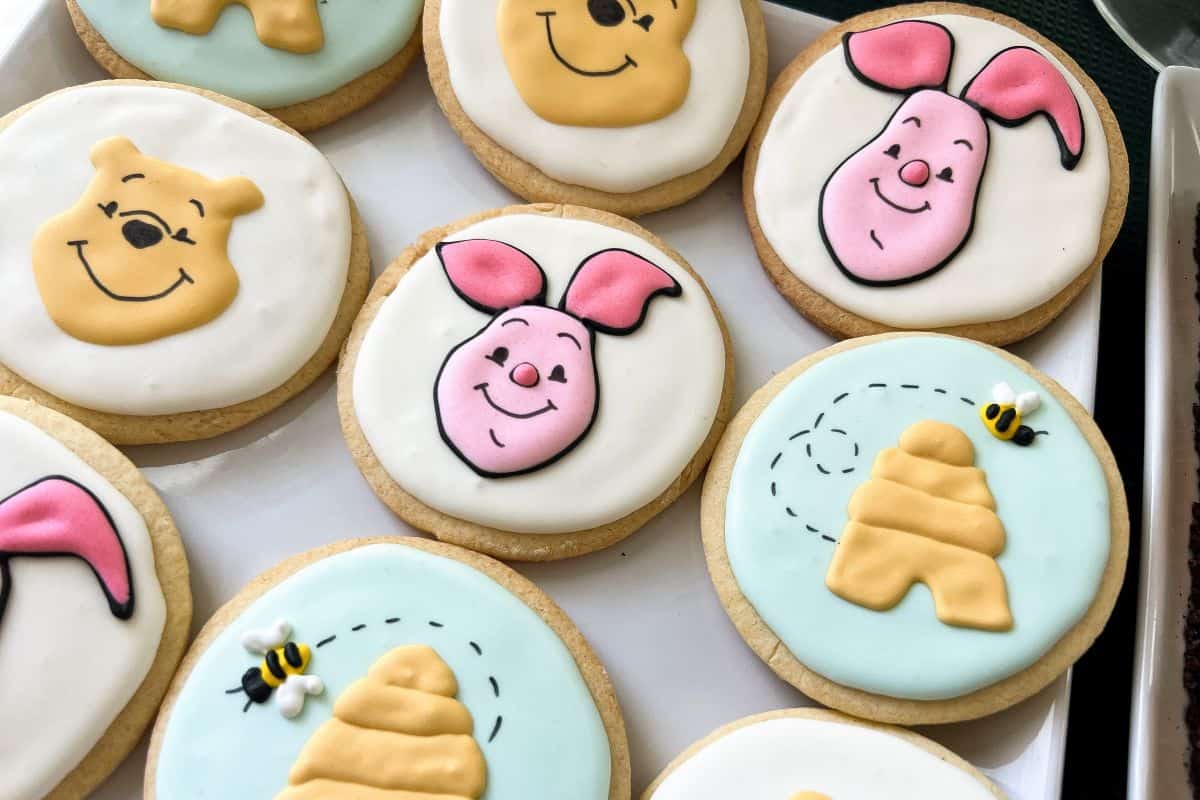 a piglet face sugar cookie on a white plate with other Winnie the Pooh themed cookies