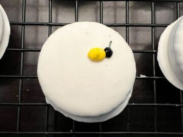 a yellow oval of royal icing next to a black dot of royal icing on a white fudge covered Oreo