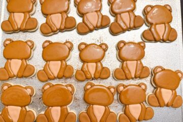 a tray of teddy bear cookies with royal icing before the faces and paws have been added