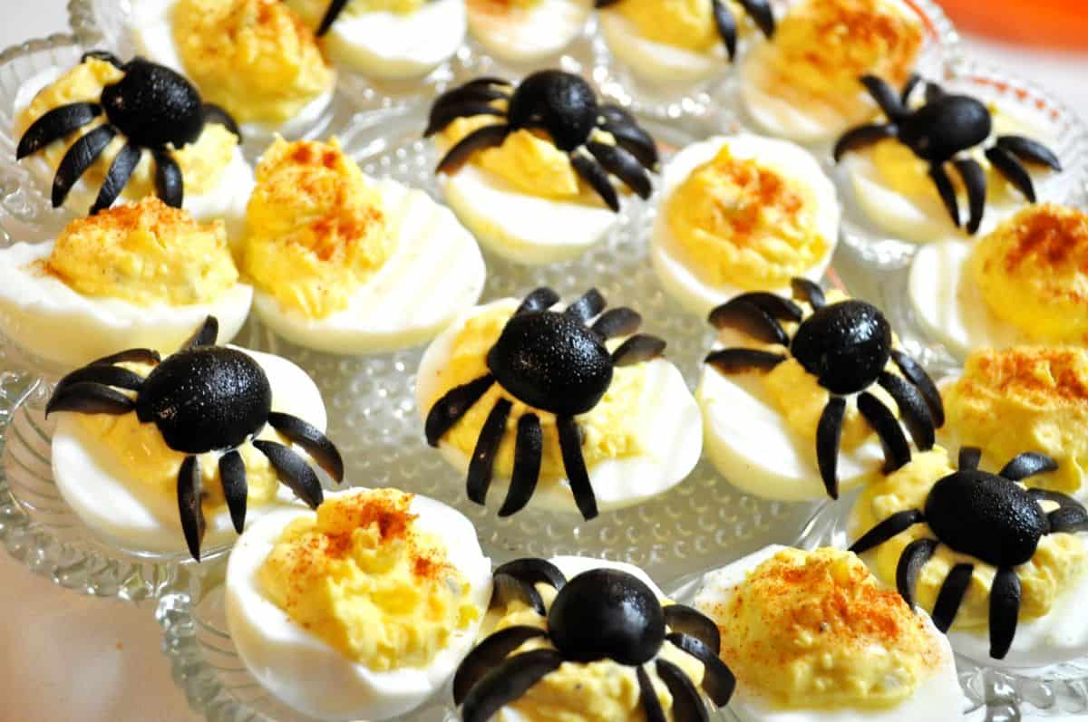 Halloween deviled eggs with black olive spiders on a glass platter
