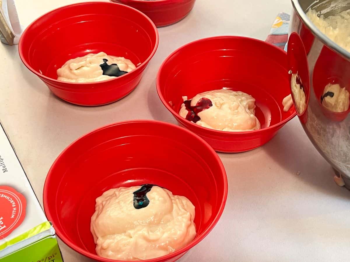bowls of cake batter with food coloring gel on top of the mounds of batter