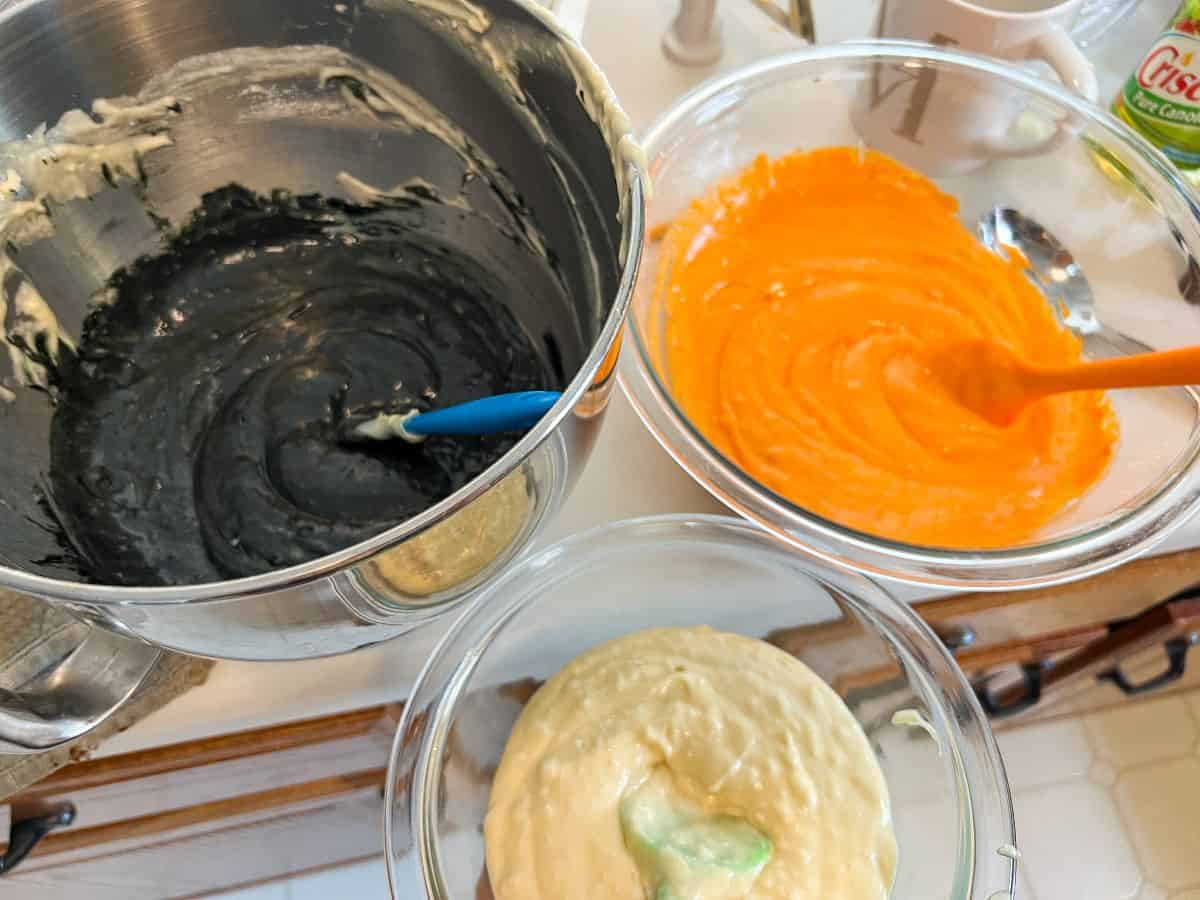 three bowls of cake batter in untinted, black and orange