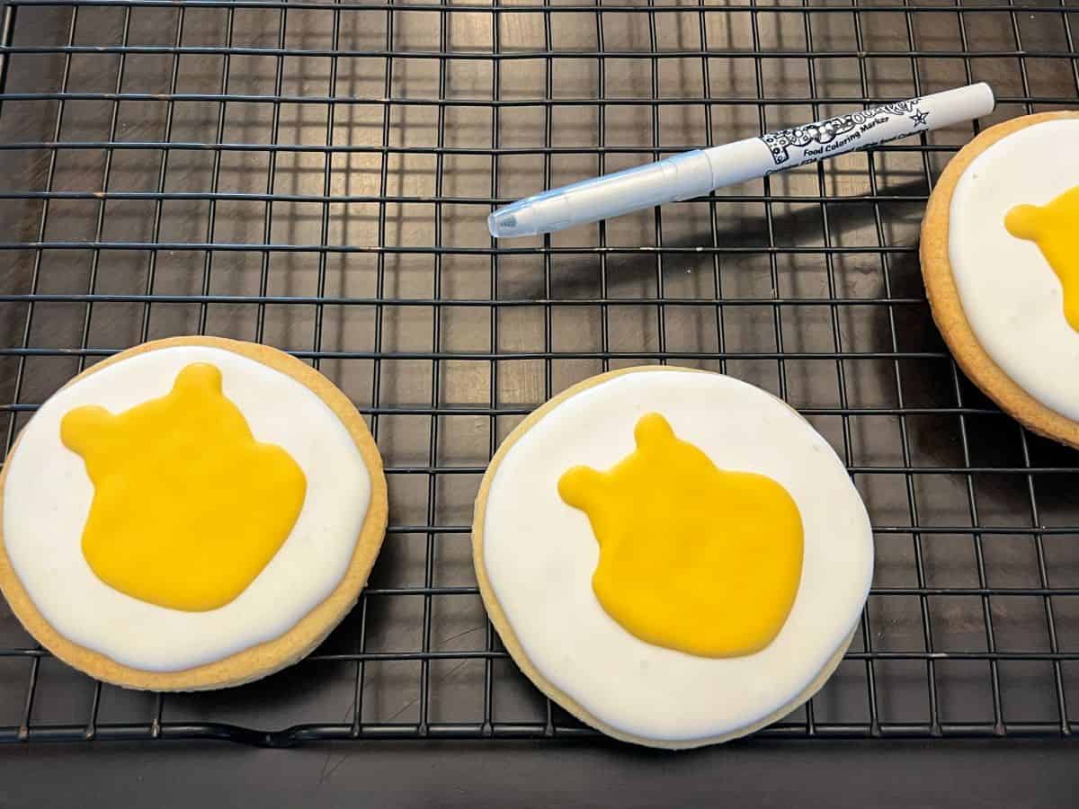 yellow royal icing in the shape of Winnie the Pooh's face on a white cookie