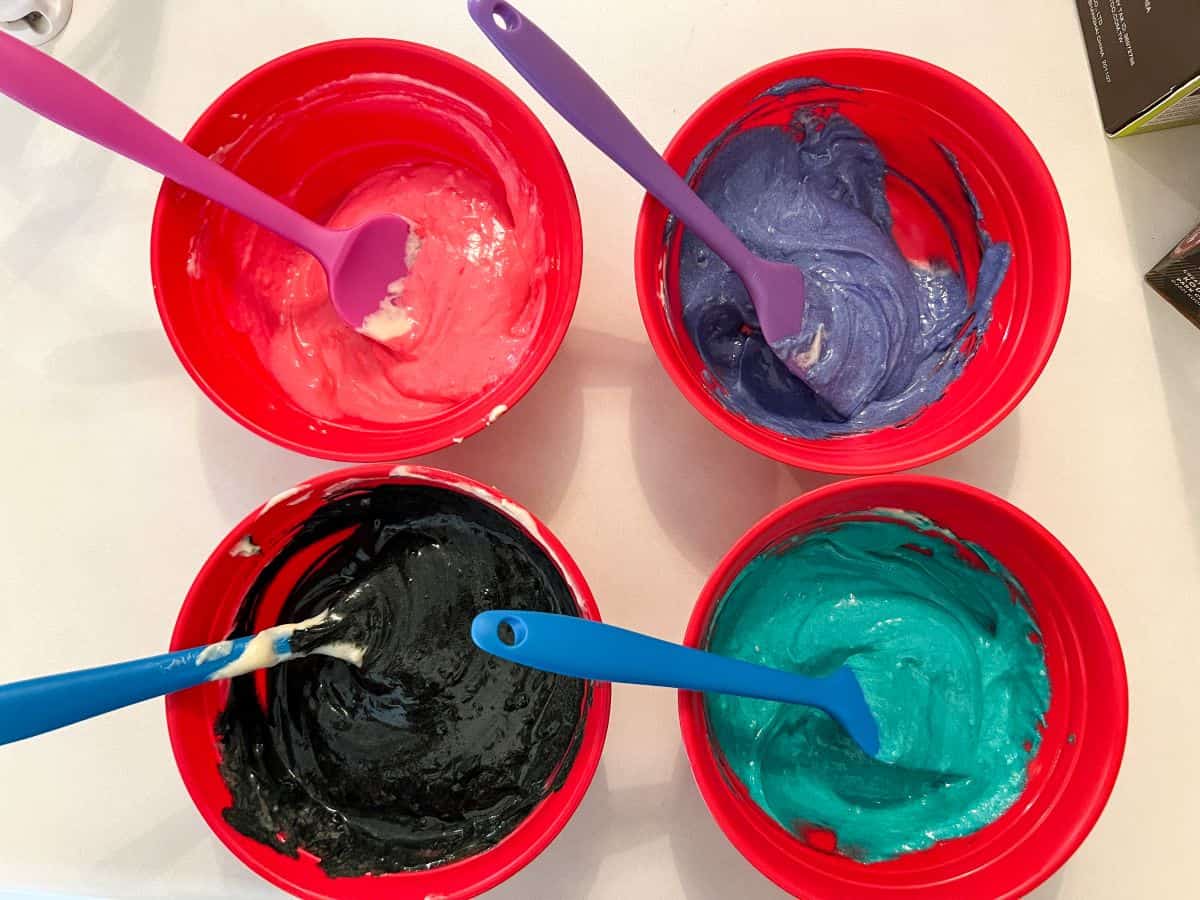 4 bowls of colored cake batter with small silicone spatulas