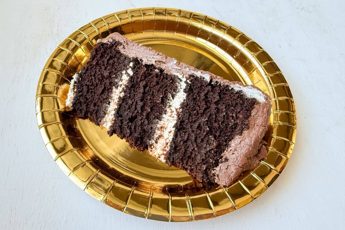 a slice of 3 layer chocolate cake on a gold paper plate