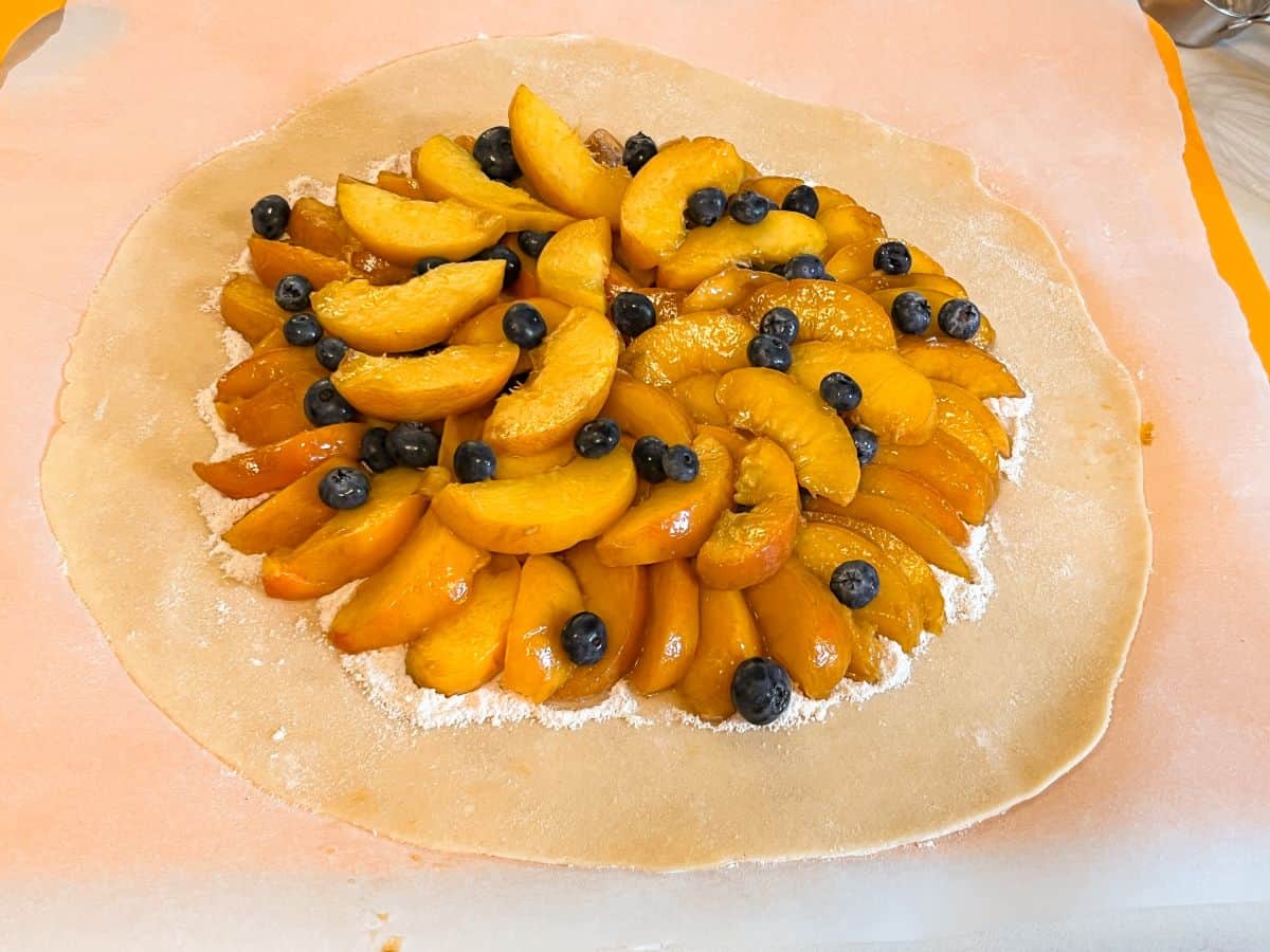 slices of peaches arranged in a circle on a pie crust with fresh blueberries evenly sprinkled over the peaches
