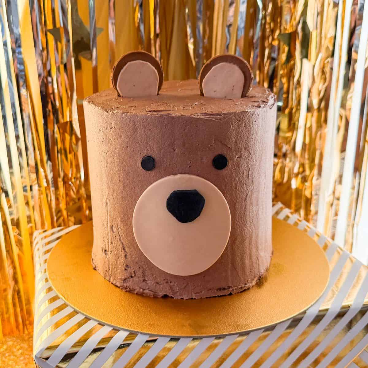 a chocolate teddy bear cake on a gold cardboard cake board on top of a wrapped box