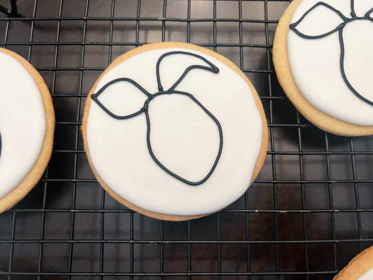black royal icing outline of piglet's face and ears on a white royal icing cookie
