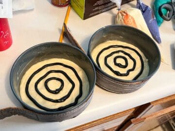 light yellow cake batter in round cake pans with back concentric circles of cake batter piped on top