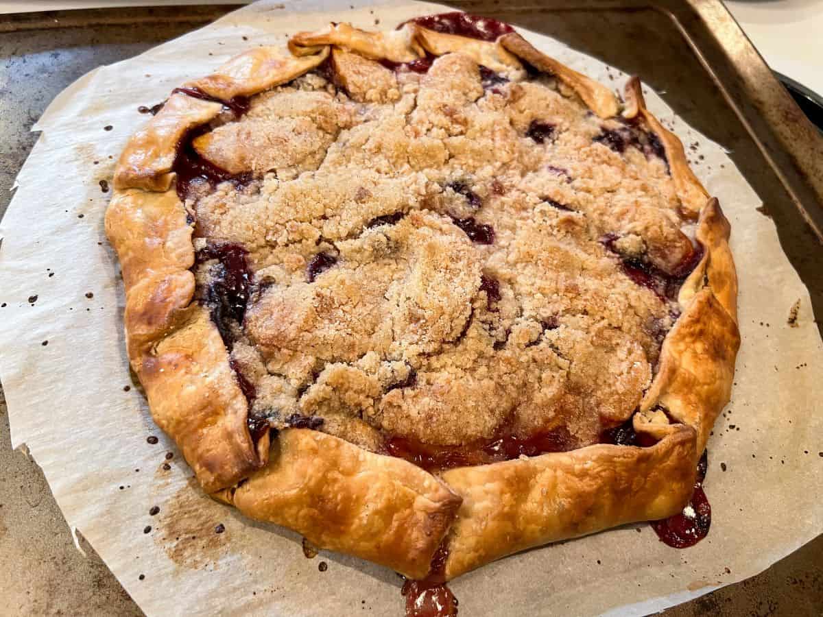 a baked blueberry peach tart on a piece of parchment on top of a cookie sheet