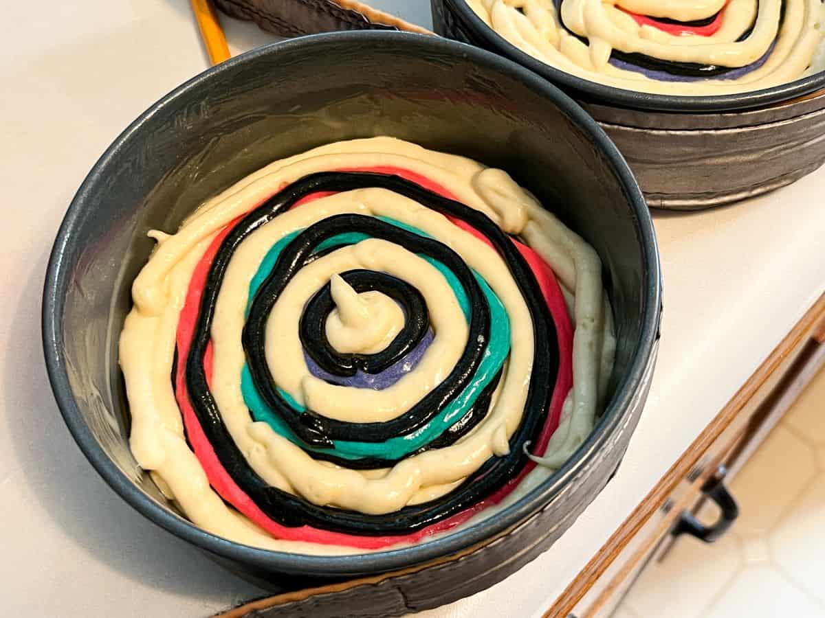 black cake batter piped over colored cake batter in a round pan
