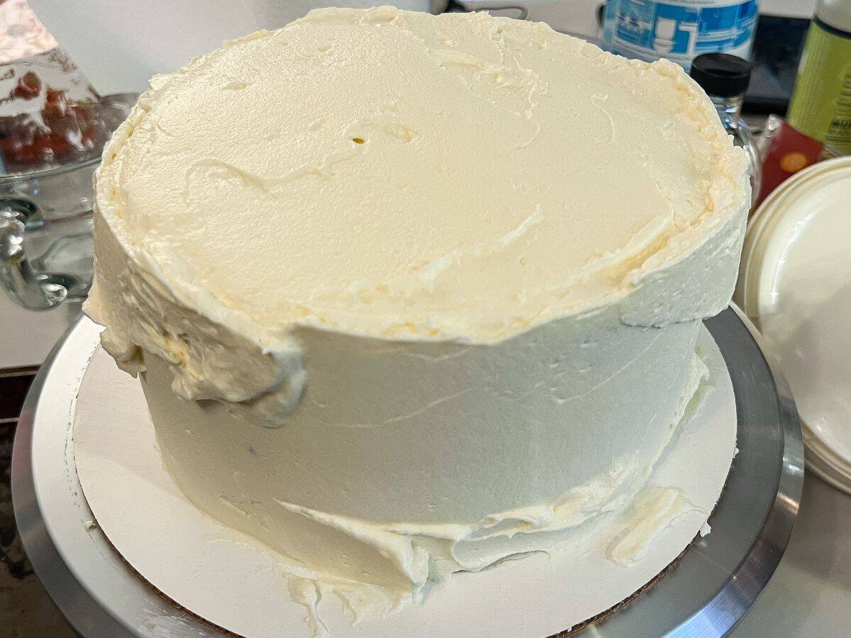 a 3 layer carrot cake covered in cream cheese frosting with clumps of frosting to cover gaps
