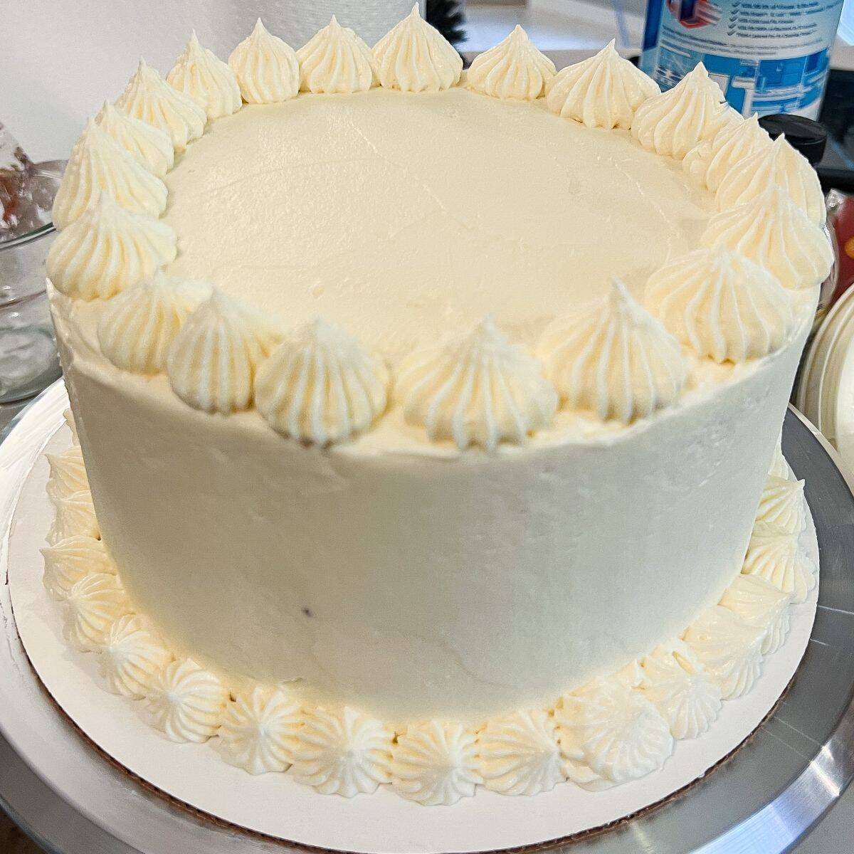 a 3 layer carrot cake covered in cream cheese frosting with decorate piped frosting around the top and bottom border of the cake