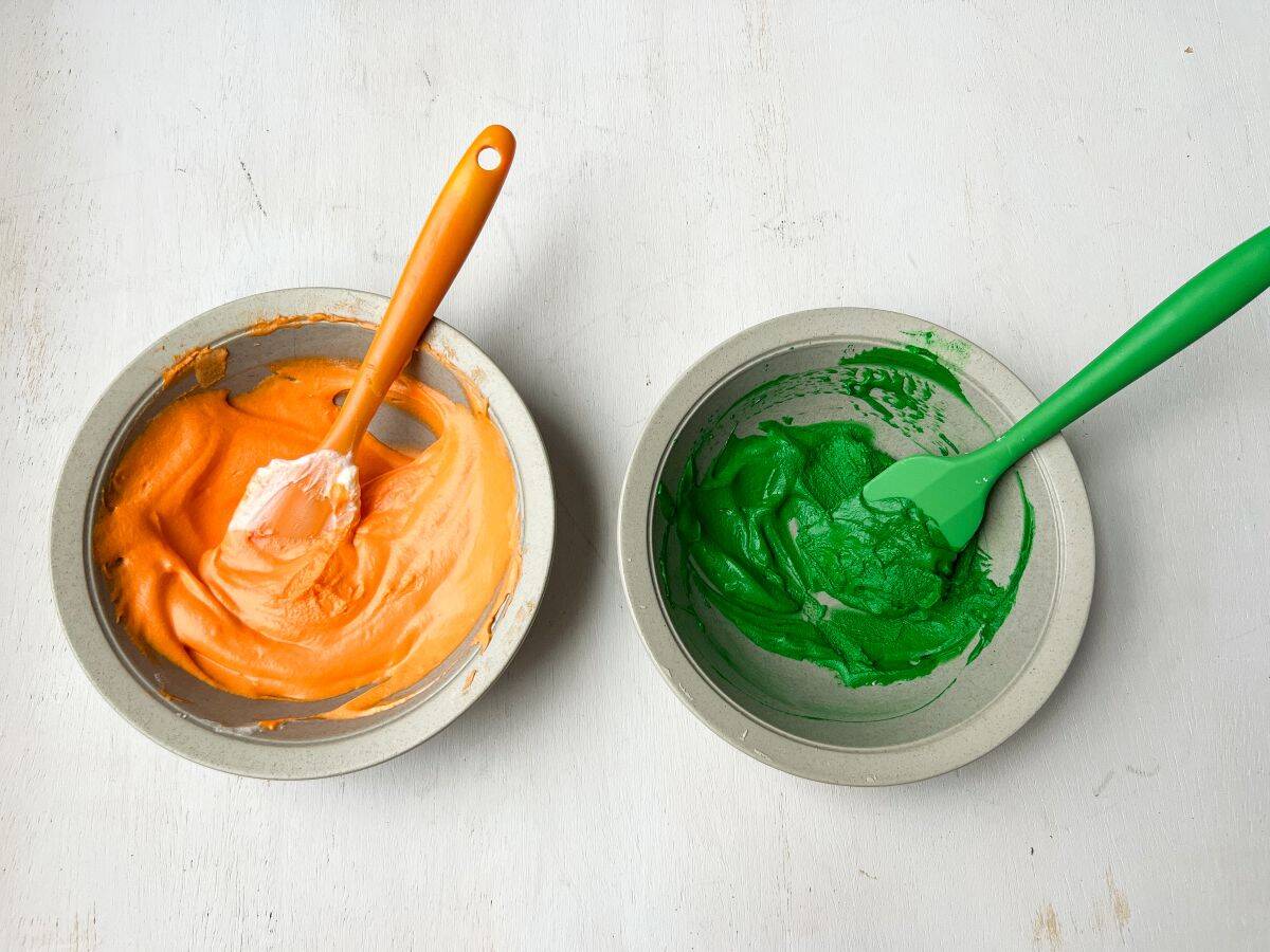 two bowls of cream cheese frosting: one colored orange and one colored green.