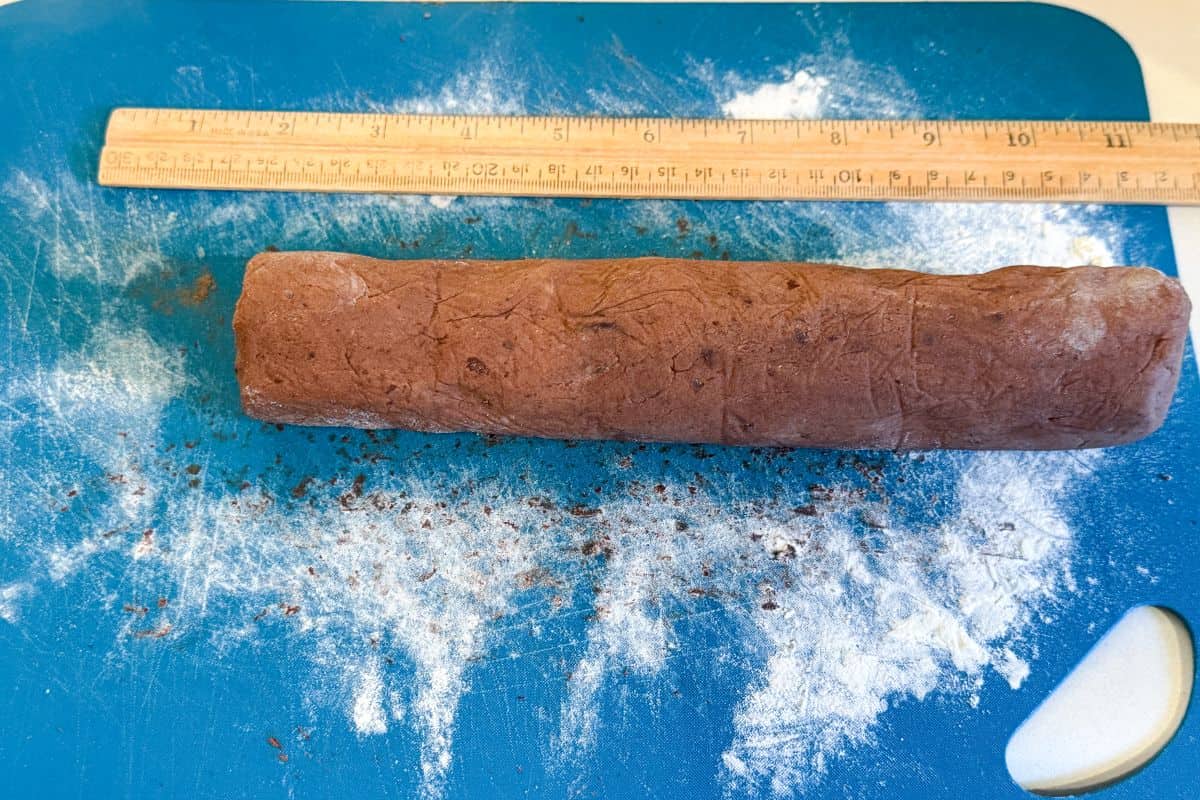 a log of chocolate cookie dough on a blue cutting mat with a wooden ruler next to it