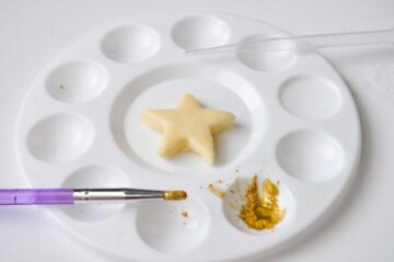 gold luster dust in the well of a paint palette with an iced cookie in the center