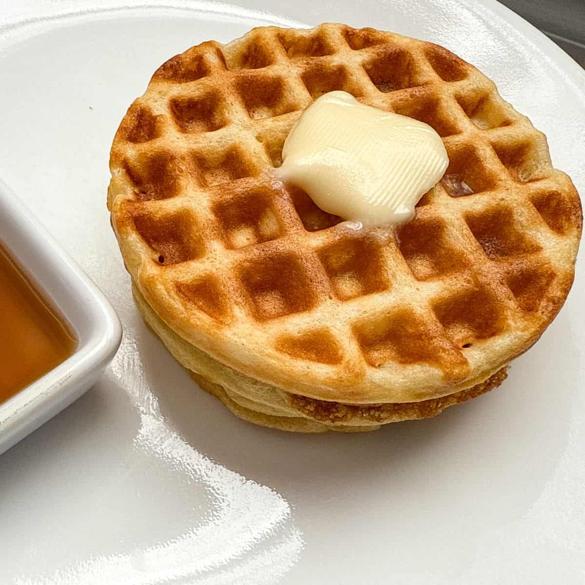 round buttermilk waffles stacked on a white plate with butter on top