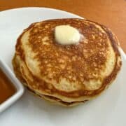 fluffy buttermilk pancakes on a white plate with butter on top