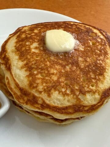 fluffy buttermilk pancakes on a white plate with butter on top