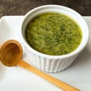 Nut Free Pesto in a white ramekin on a white plate with a wooden scoop next to it