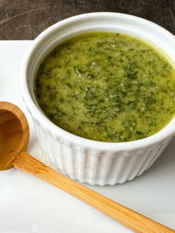 Nut Free Pesto in a white ramekin on a white plate with a wooden scoop next to it