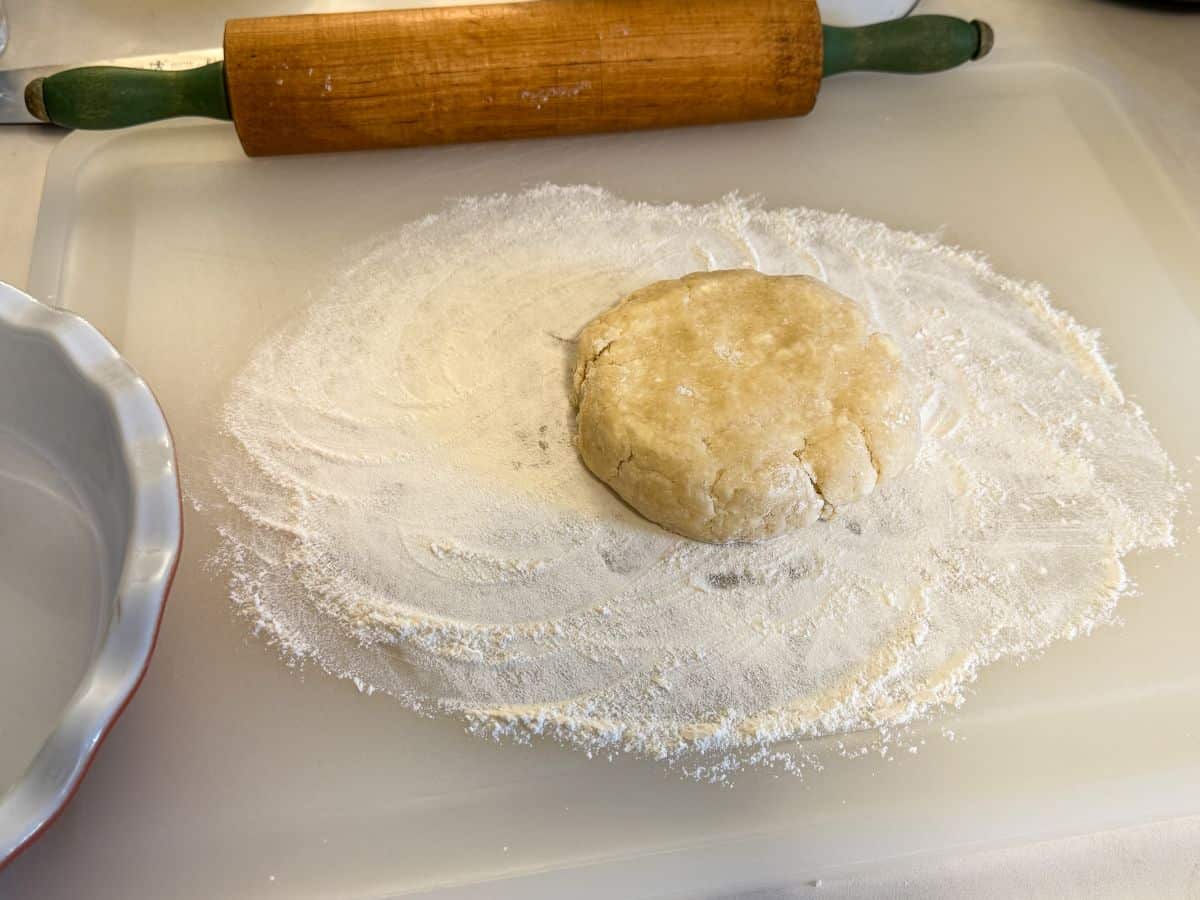 a disc of pie dough on a floured cutting board next to a wooden rolling pin