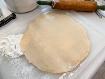 dough rolled out thin on a floured cutting board next to a rolling pin
