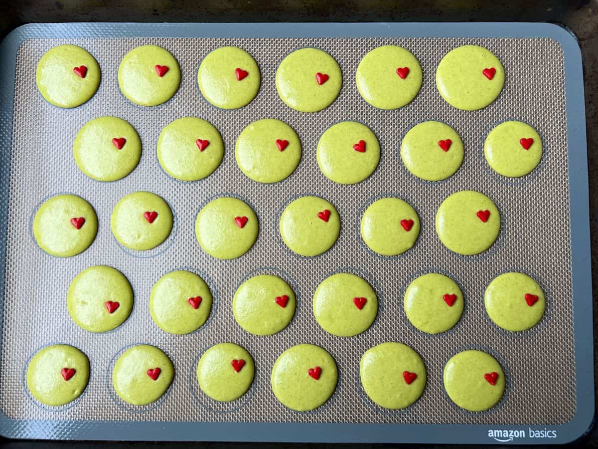 lime green colored macarons piped on a macaron mat with little red heart sprinkles