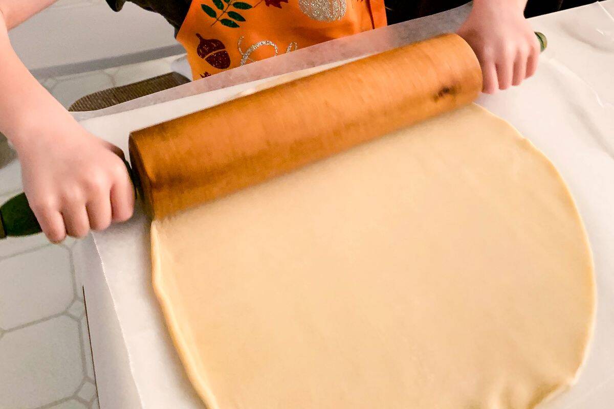 a child's hands rolling a pie crust with a rolling pin