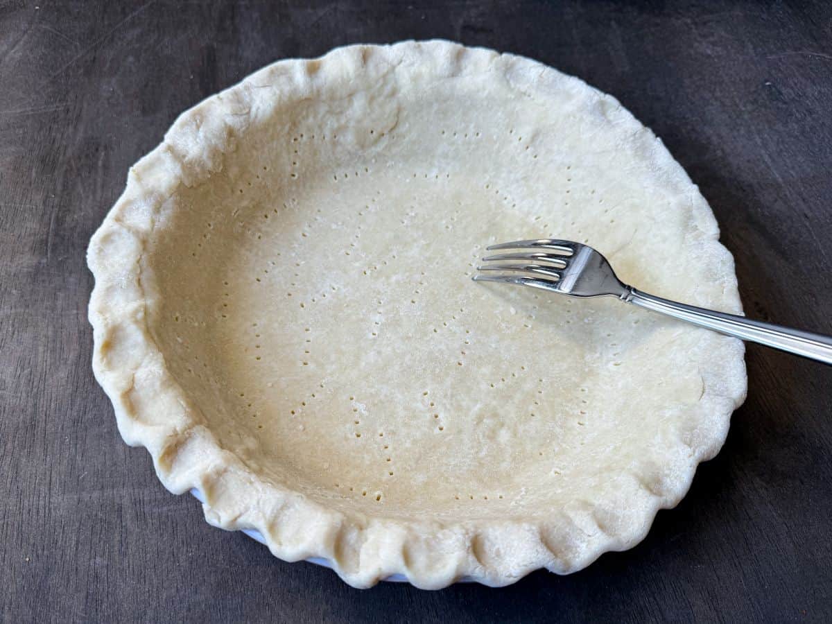 pie dough fitted into a pie plate with a fork in it and prick marks from the fork