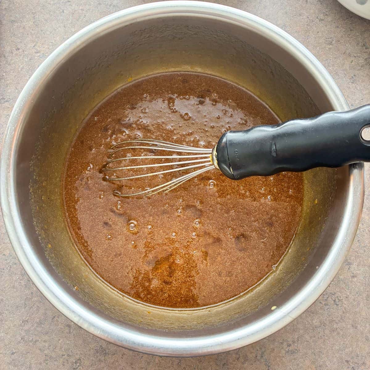 pecan pie filling in a bowl with a whisk next to a bag of pecans and a measuring cup filled with pecans