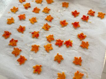 painted pie crust leaves spread out on a parchment lined cookie sheet