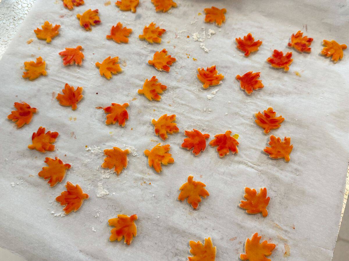painted pie crust leaves spread out on a parchment lined cookie sheet