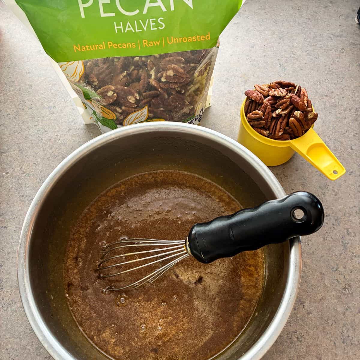 pecan pie filling in a bowl with whisk next to a bag of pecans and a measuring cup filled with pecans