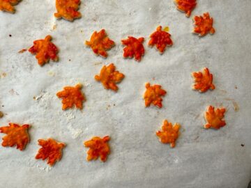 painted pie crust leaves spread out on a parchment lined cookie sheet