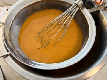 pumpkin pie filling being strained through a fine mesh sieve