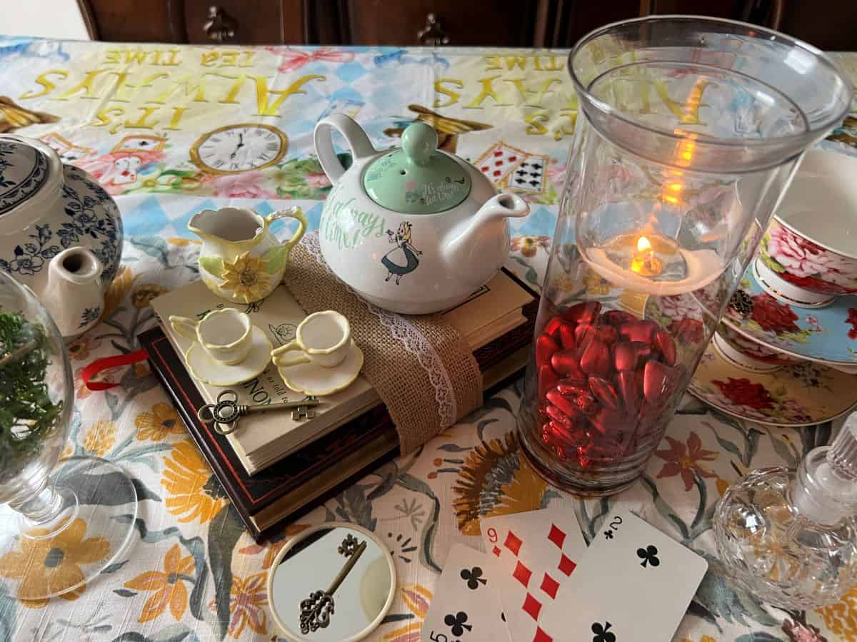 books stacked up with lace and a small teapot and teacups on top next to a candle holder