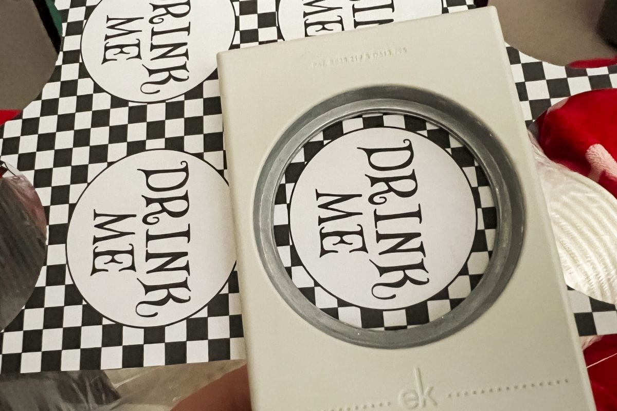 a circular punch cutting out the words "Drink Me" from adhesive label paper
