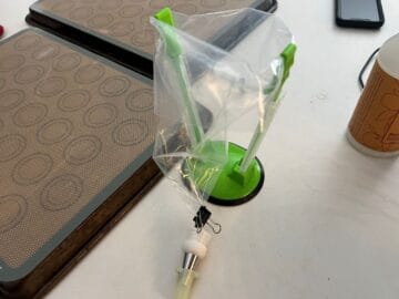 an empty piping bag in a holder with a binder clip holding the opening closed
