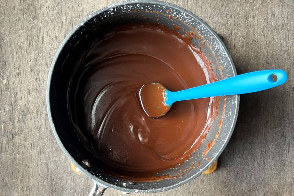 hot fudge sauce in a small saucepan with a blue silicone spatula