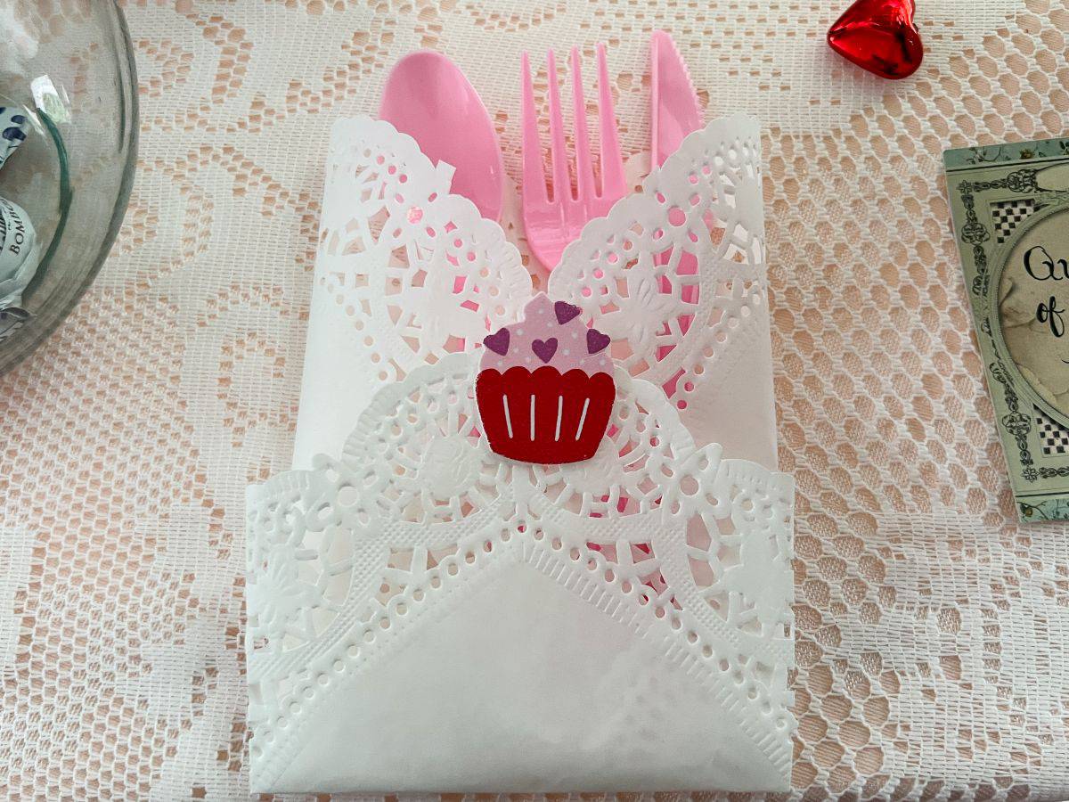 a paper doily folded up with pink plastic cutlery inside and sealed with a Valentine sticker