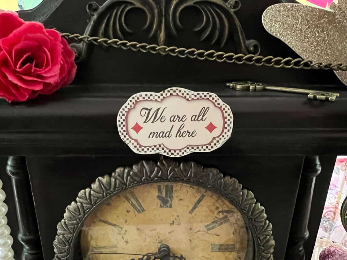 a sign on a clock that says "We're all Mad Here"