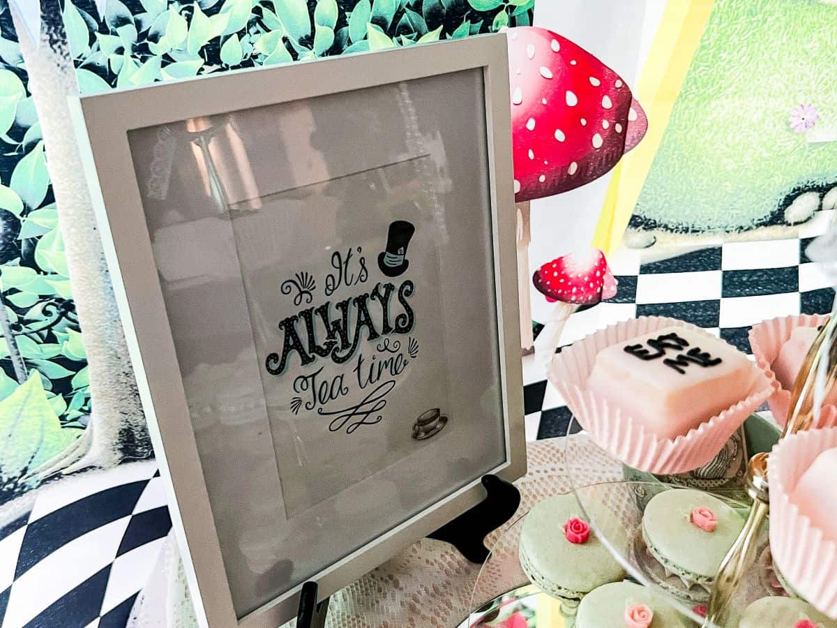 a framed sign that reads "It's always tea time" on a dessert table