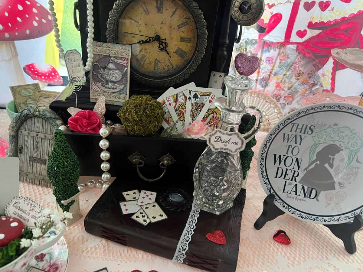 a glass bottle labeled "Drink me" on top of an antique book next to a wooden antique clock