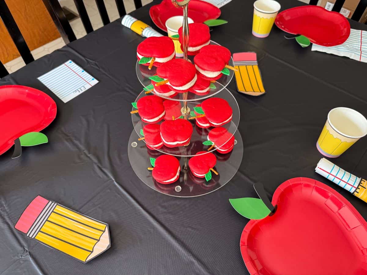 a table set with apple paper plates and a 3 tiered server with apple macarons in the center