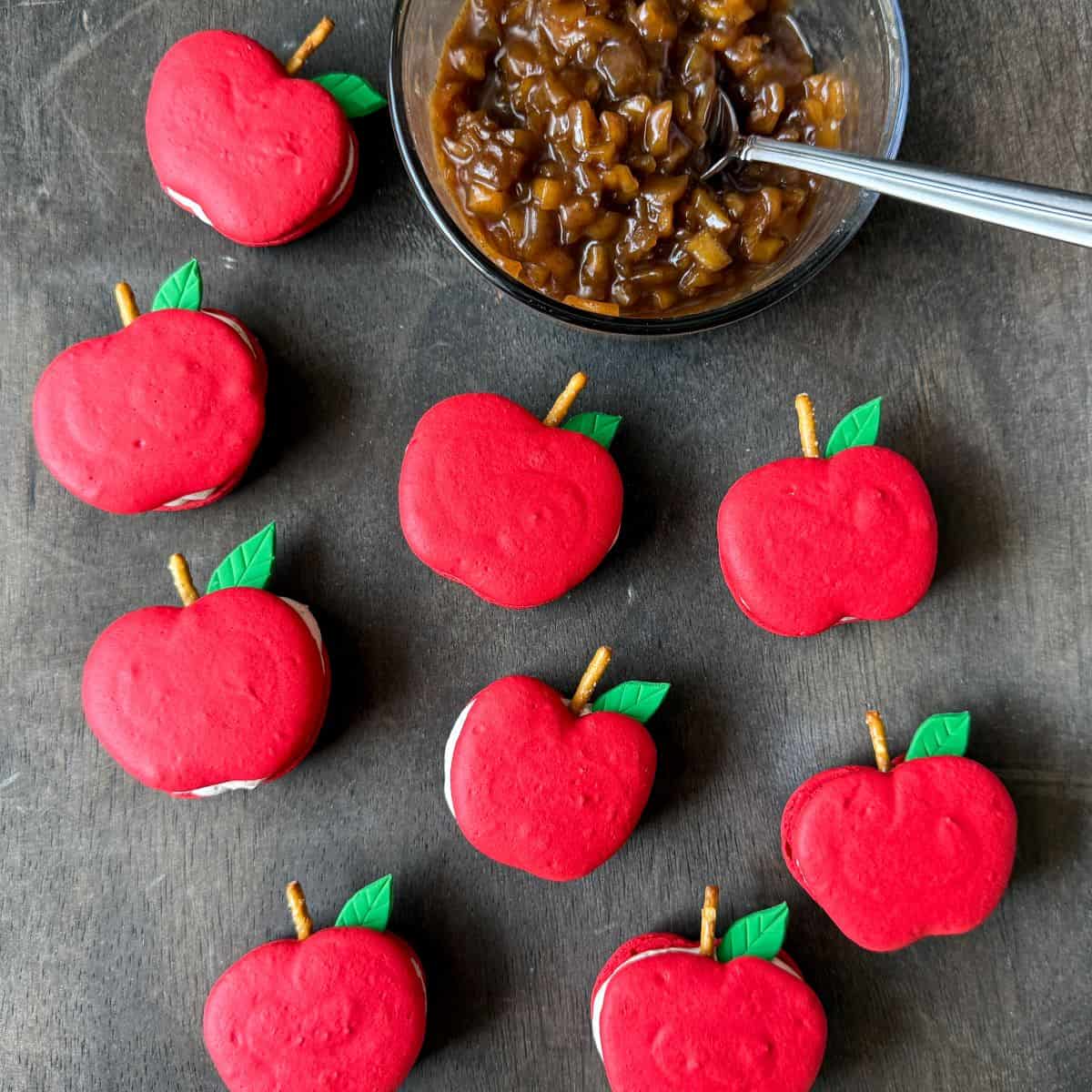 caramel apple cider macarons on a dark wood table with a bowl of caramel apple filling