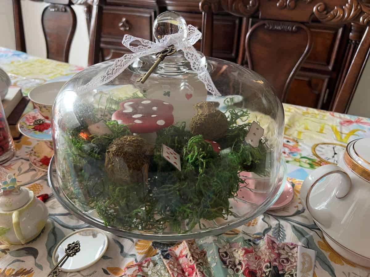 a glass domed cake stand with moss and mushroom figurines inside