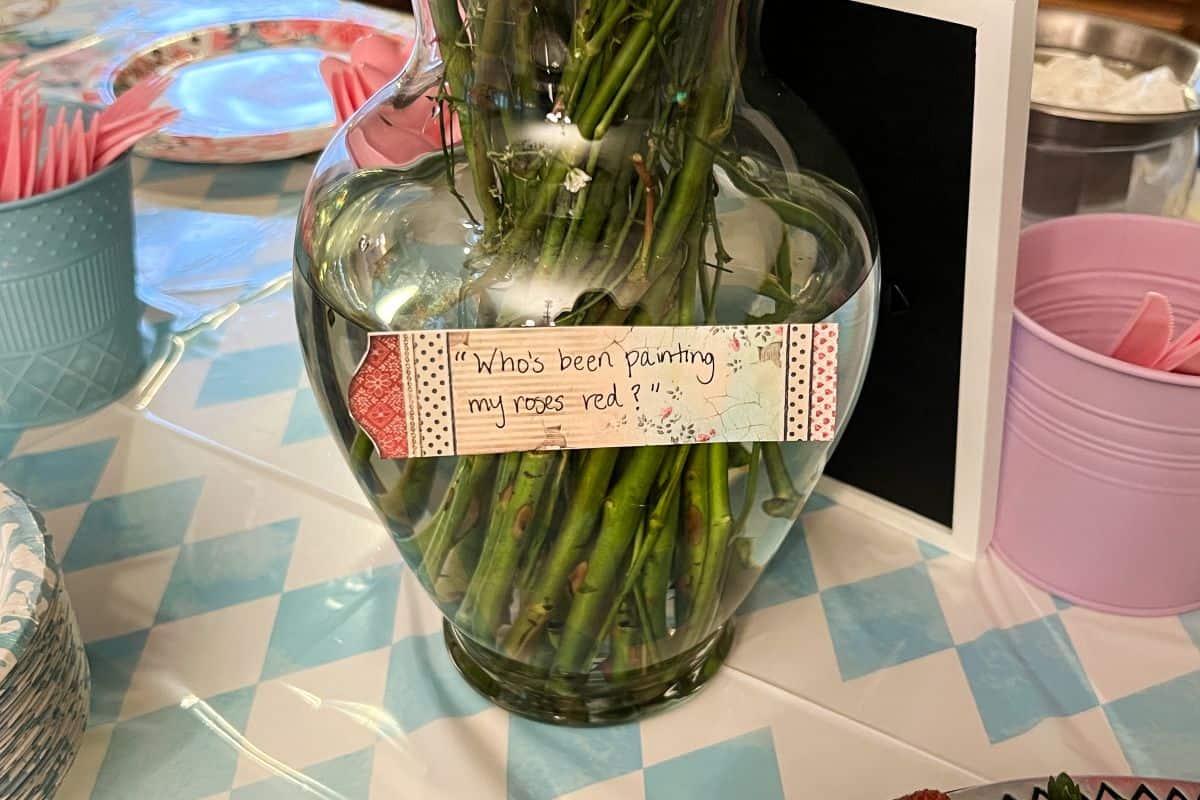 a label on a vase of roses that says "who's been painting the roses red?"